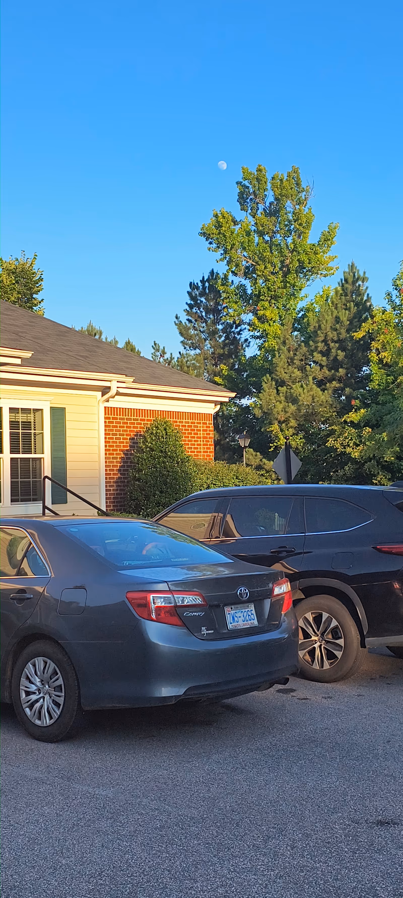 Parking lot in front of a brick and cream senior living building with trees and cars.