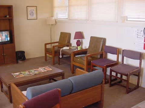 A small senior living lounge with seating, magazines, a TV, and a coffee table.