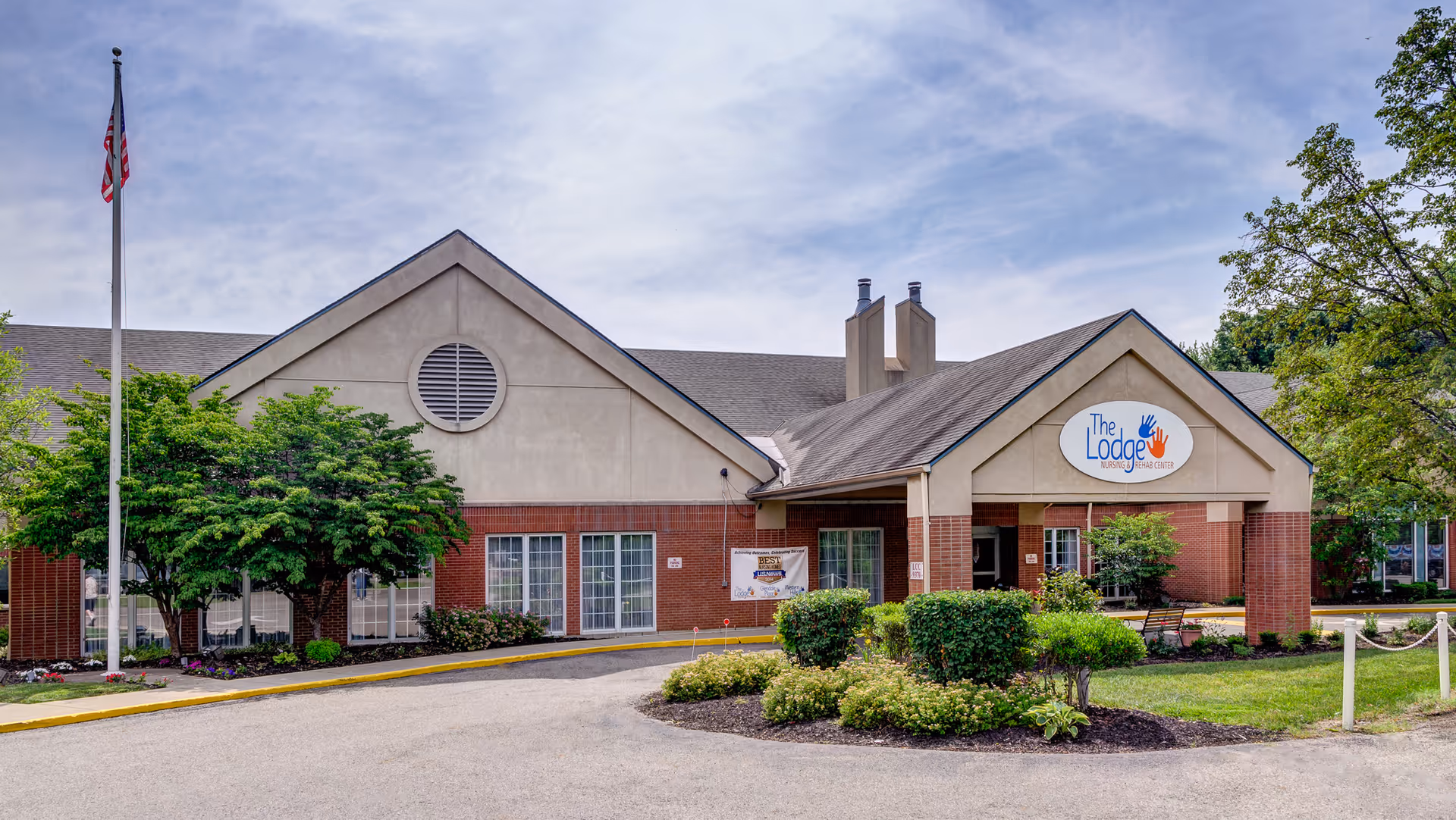 Exterior view of The Lodge Care Center building with brick facade, landscaping, and flagpole.