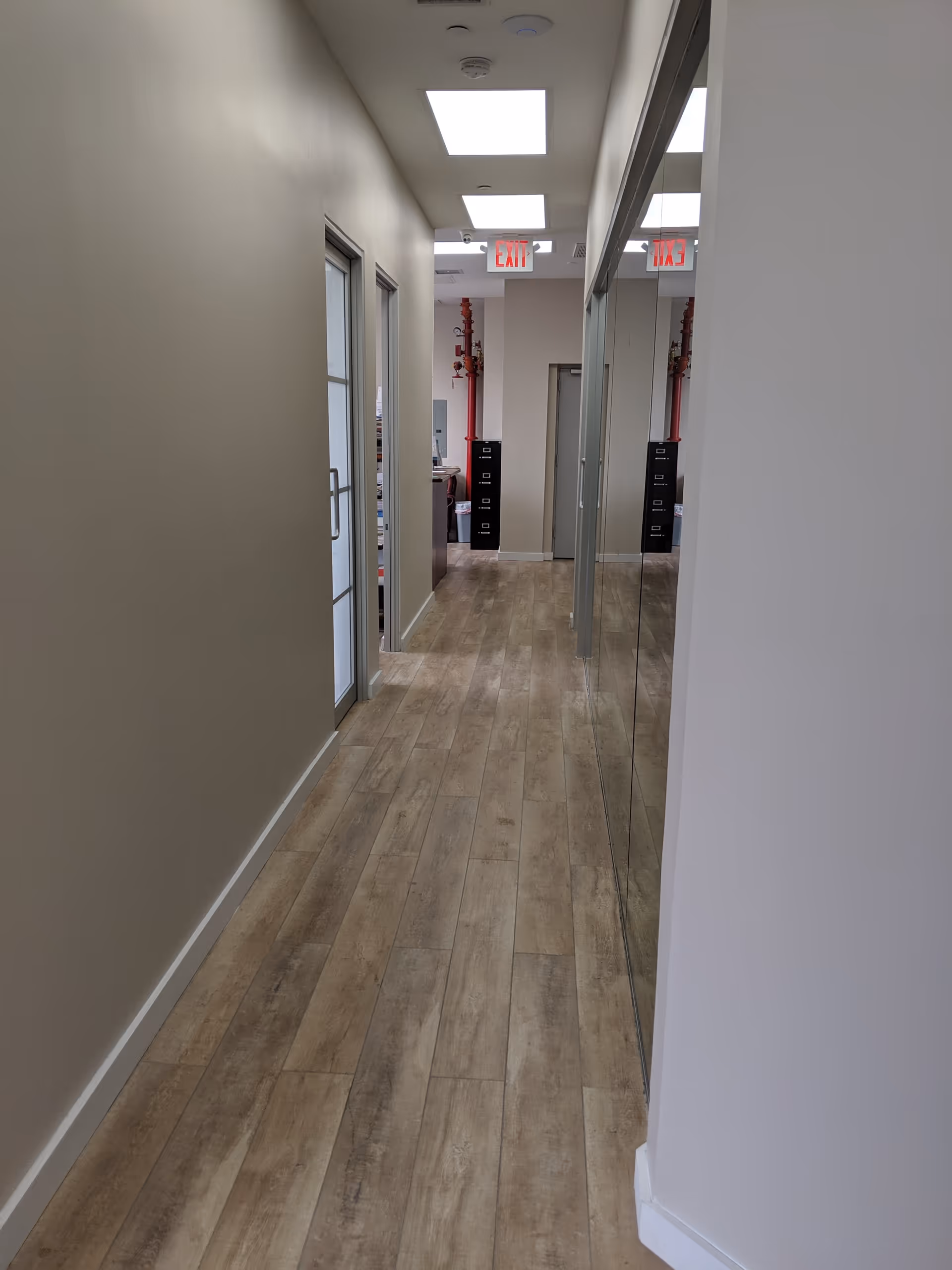 Narrow interior hallway with wood-like flooring, doors, and a mirrored wall.
