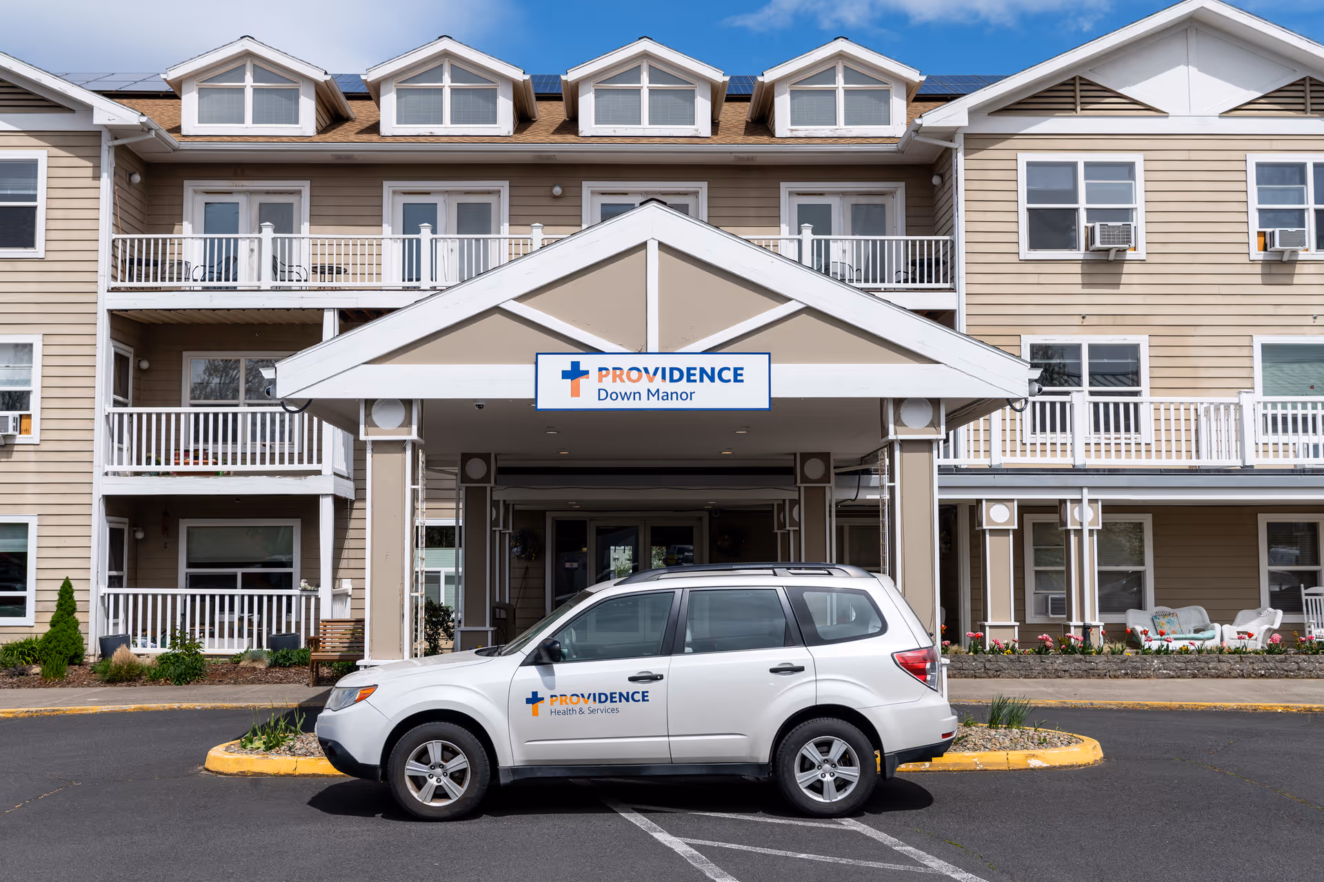 Front exterior view of Providence Down Manor building with a covered entrance and a white SUV parked in front displaying the Providence Health & Services logo.