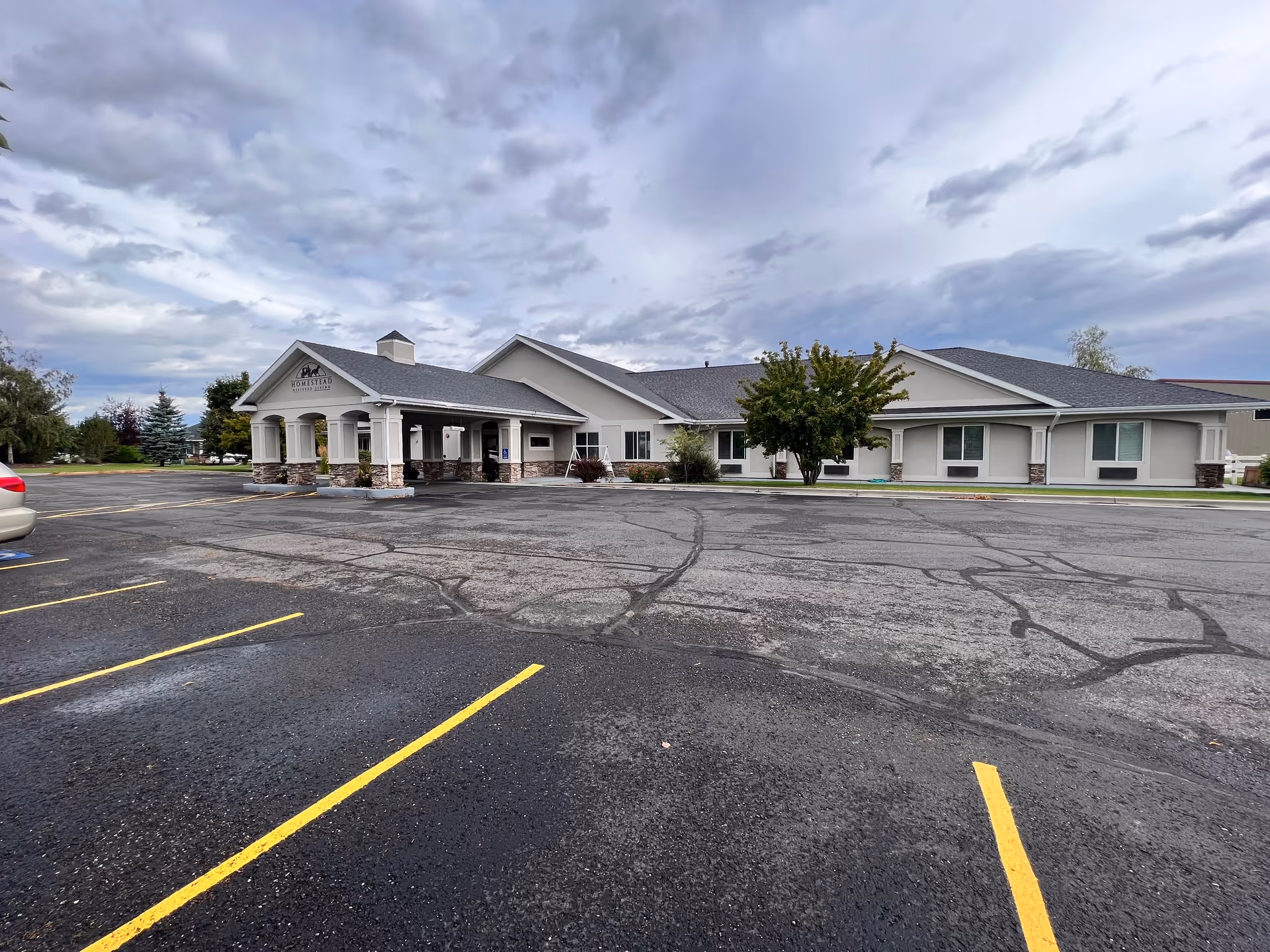 Exterior view of The Homestead Assisted Living building with a paved parking lot and cloudy sky.