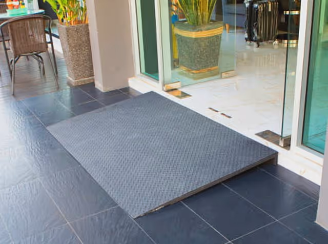 An outdoor entrance with a textured ramp leading to glass doors and potted plants.