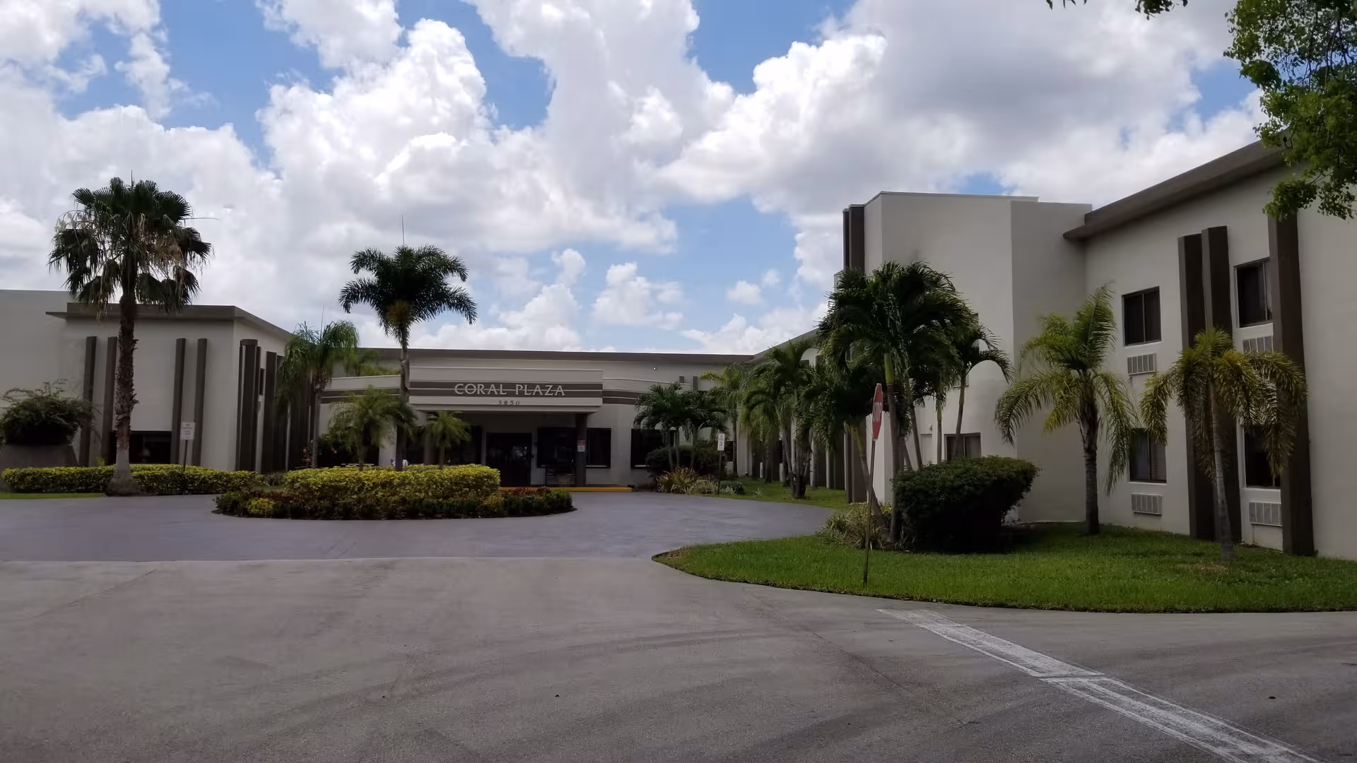 Exterior view of Coral Plaza senior living building with palm trees and a circular driveway.