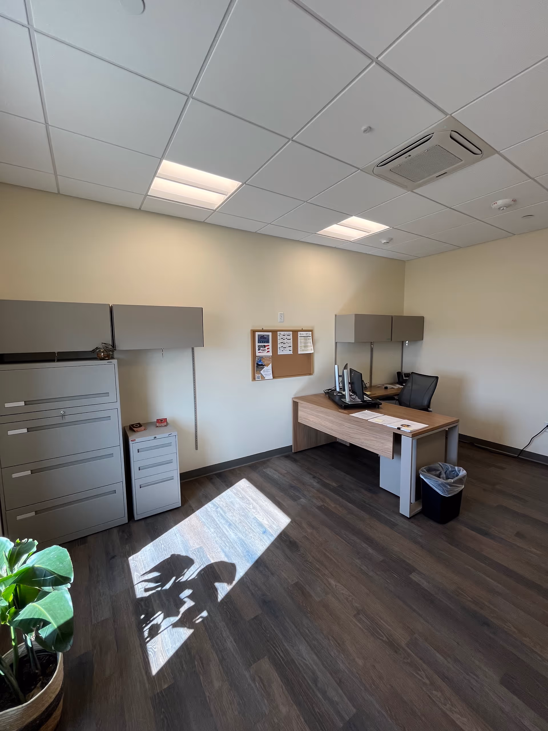Empty office in a senior living facility with desk, computer, filing cabinets, and corkboard.
