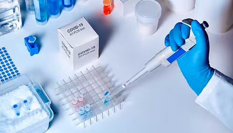 Gloved hand uses a pipette over a rack of test tubes in a laboratory.