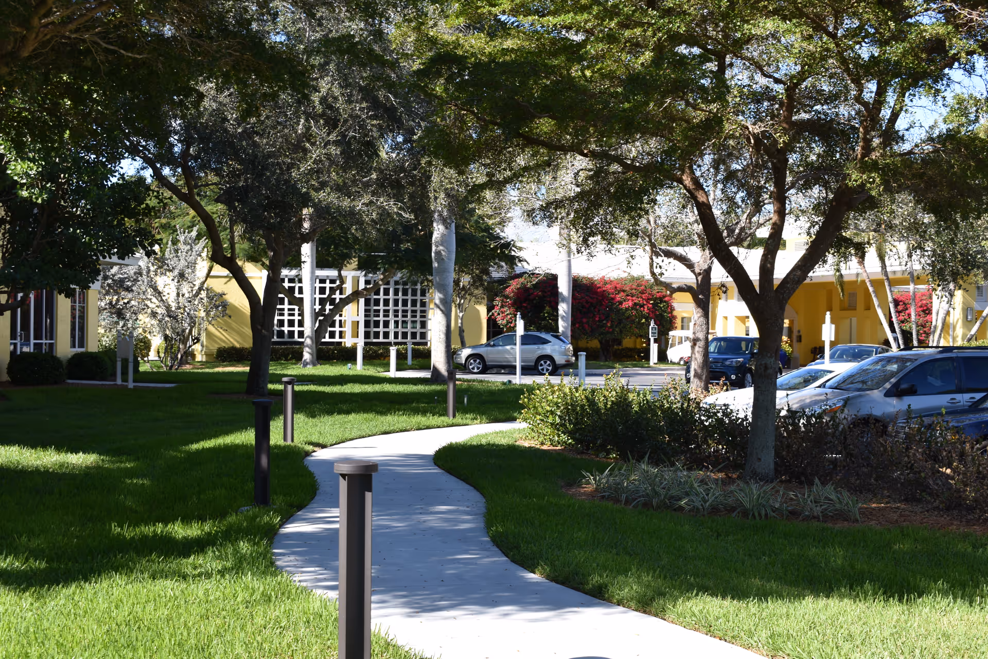 Exterior view of Cypress Cove senior living with a curved walkway, trees, and parked cars.