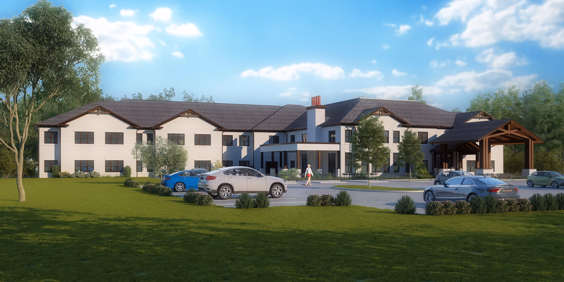 Front view of a two-story senior living facility with a covered entrance, parked cars, and landscaped lawn under a blue sky.