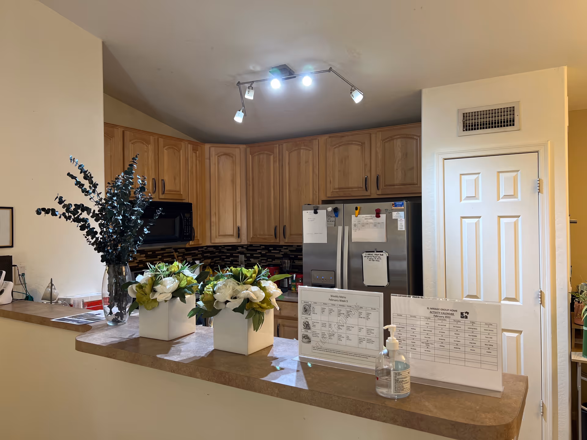 A kitchen area with wooden cabinets, stainless steel refrigerator, and flowers on the counter.