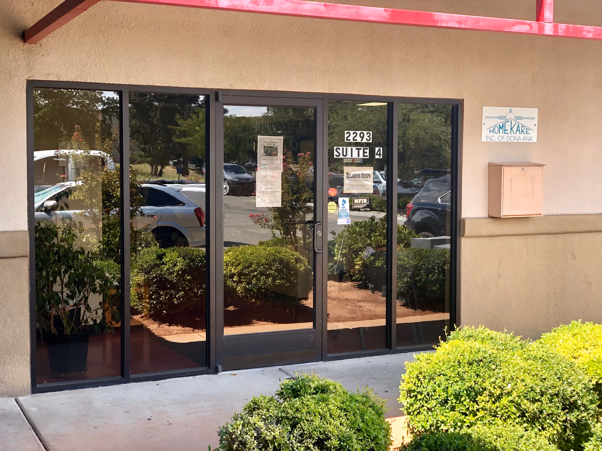 Glass front entrance of Home Kare Inc. of Dona Ana with surrounding shrubs.