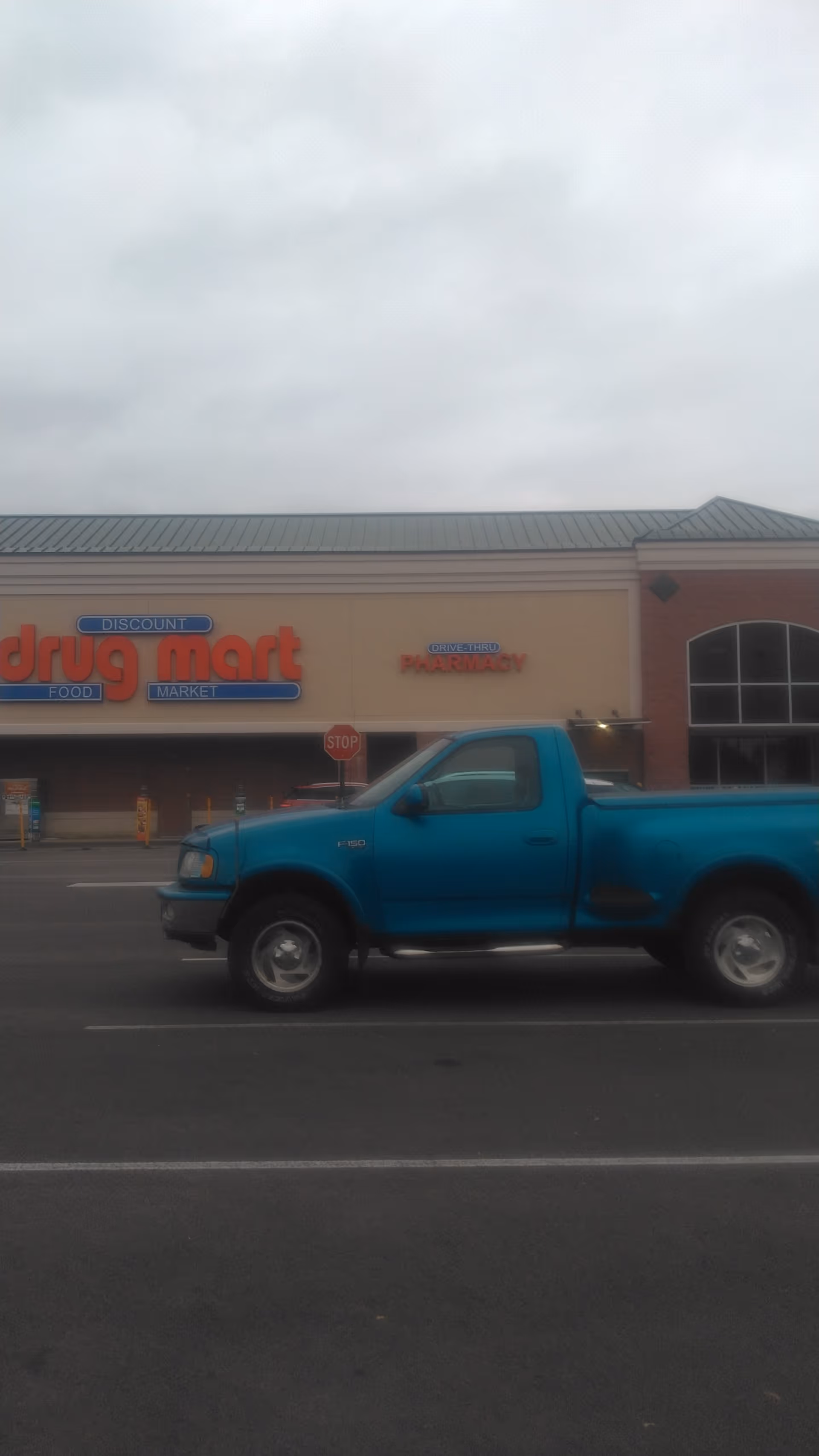 Blue pickup truck parked in front of Discount Drug Mart storefront.