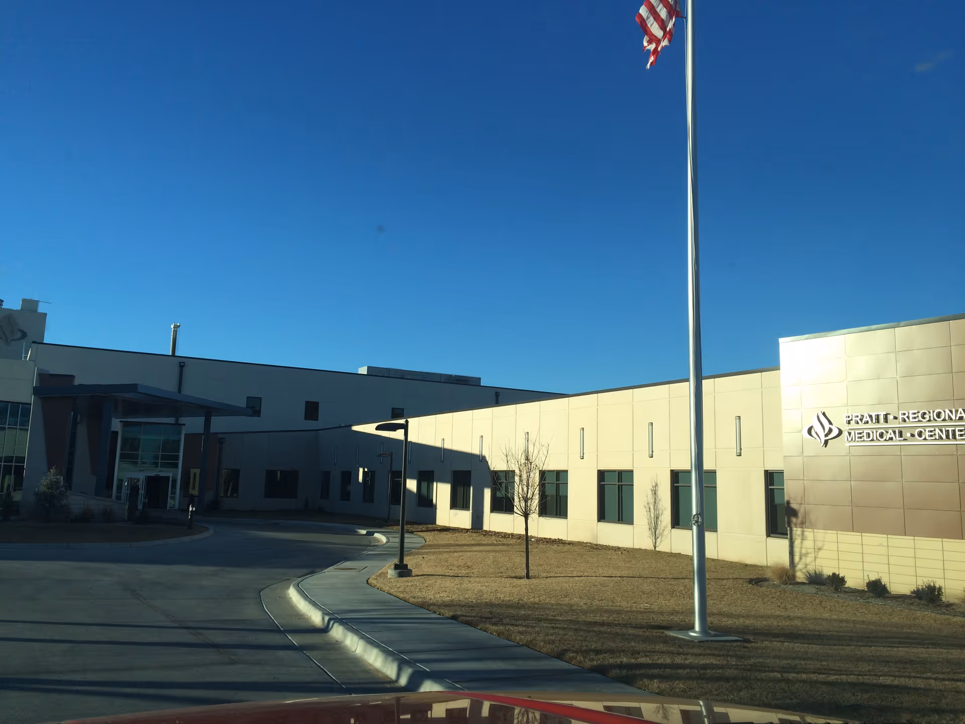 Modern Pratt Regional Medical Center exterior with flagpole, driveway, and blue sky.