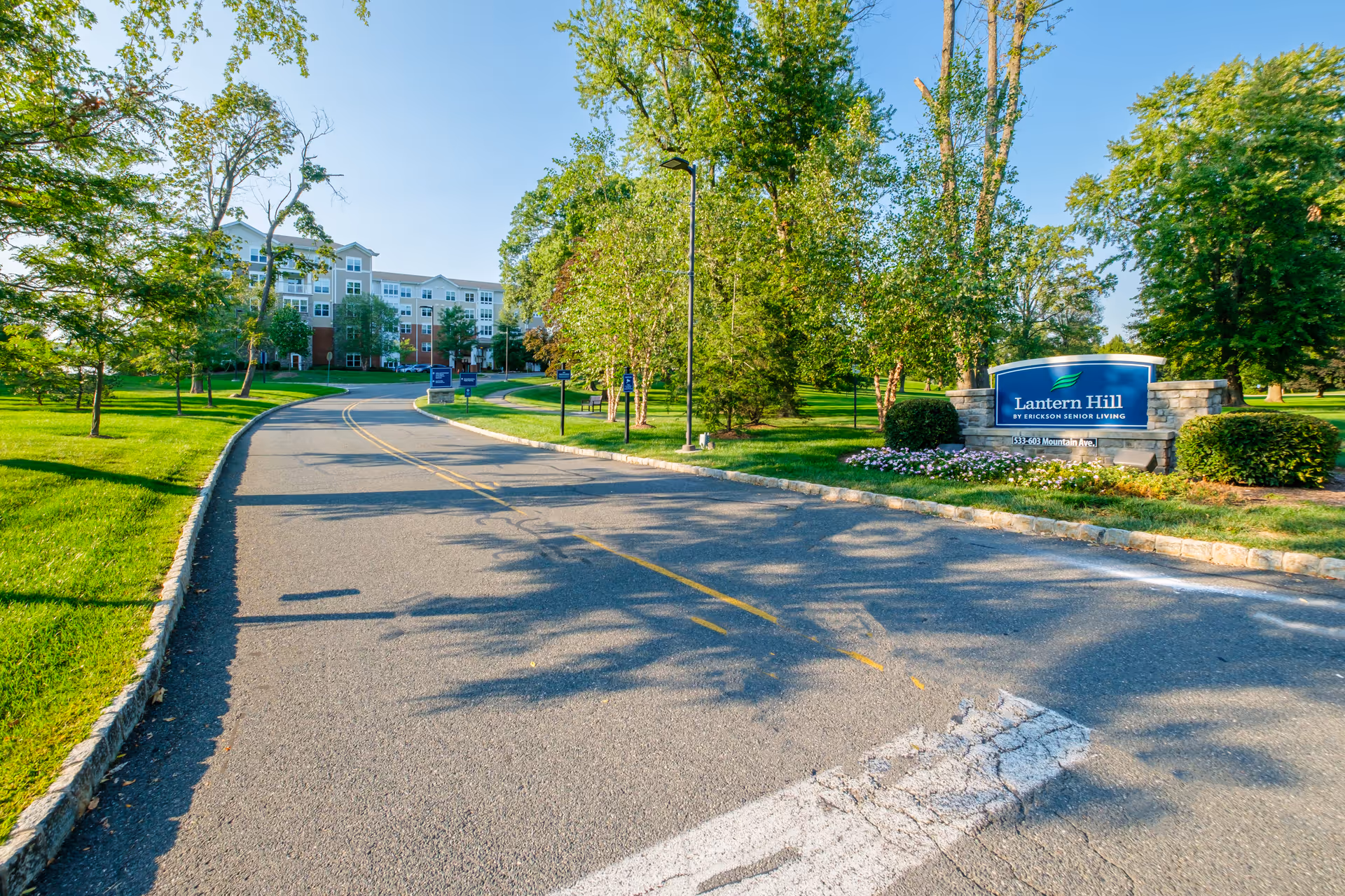 Driveway leading to the Lantern Hill senior living building with a landscaped entrance sign on the right.