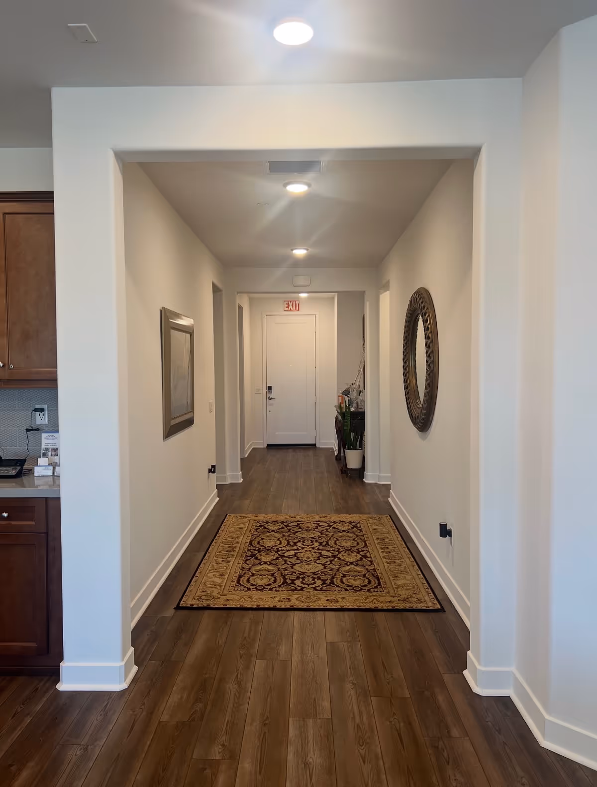 Hallway interior at Murrieta Manor: Senior Living with wood floors, rug, and wall décor.