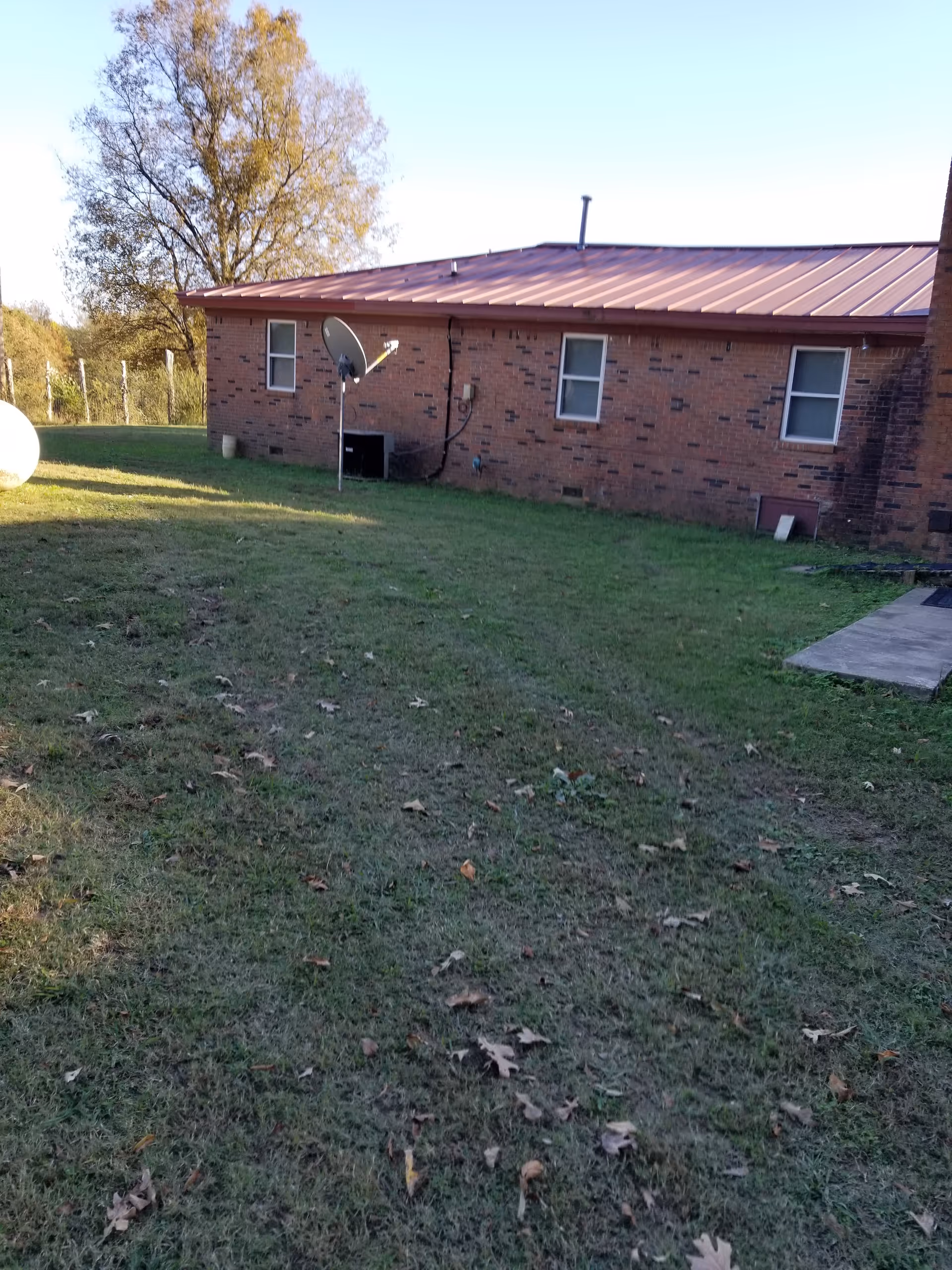 Brick building with red metal roof, satellite dish, and spacious grassy outdoor yard.