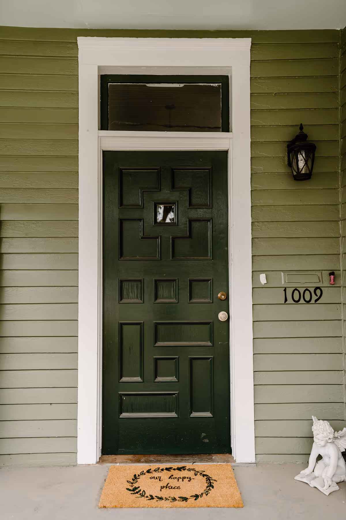 A green front door with white trim, address 1009, exterior wall, and a welcome mat.