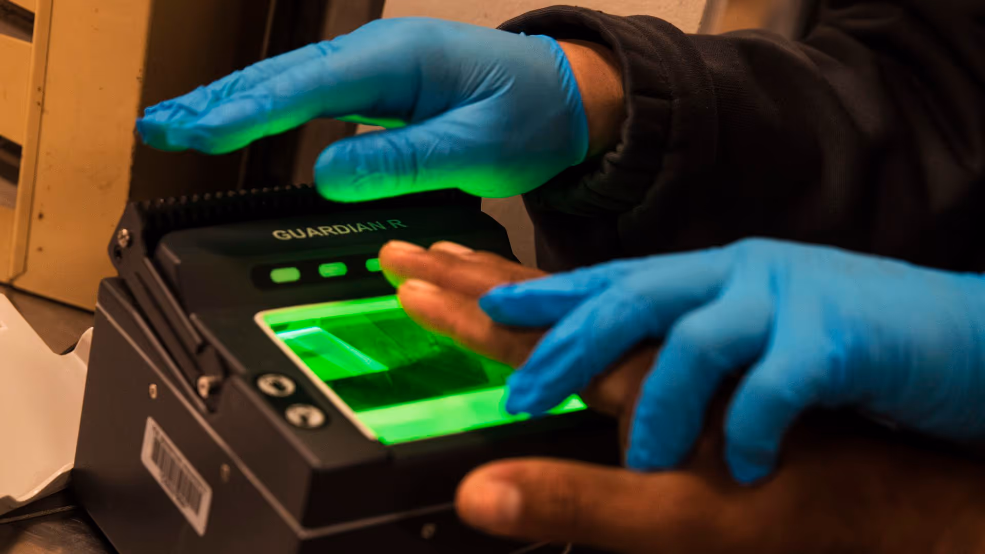 Close-up of gloved hands using a green-lit fingerprint scanner.