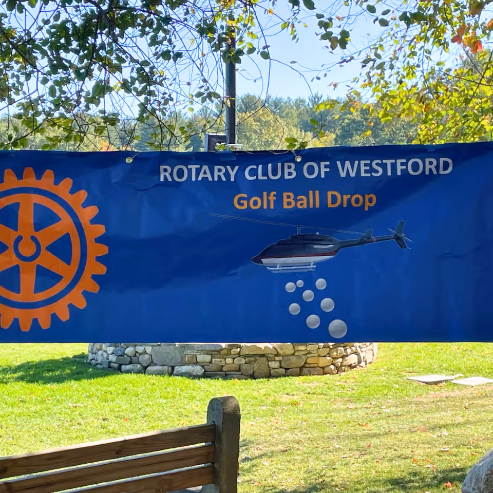 Blue Rotary banner advertising Golf Ball Drop outdoors beside a grassy area.