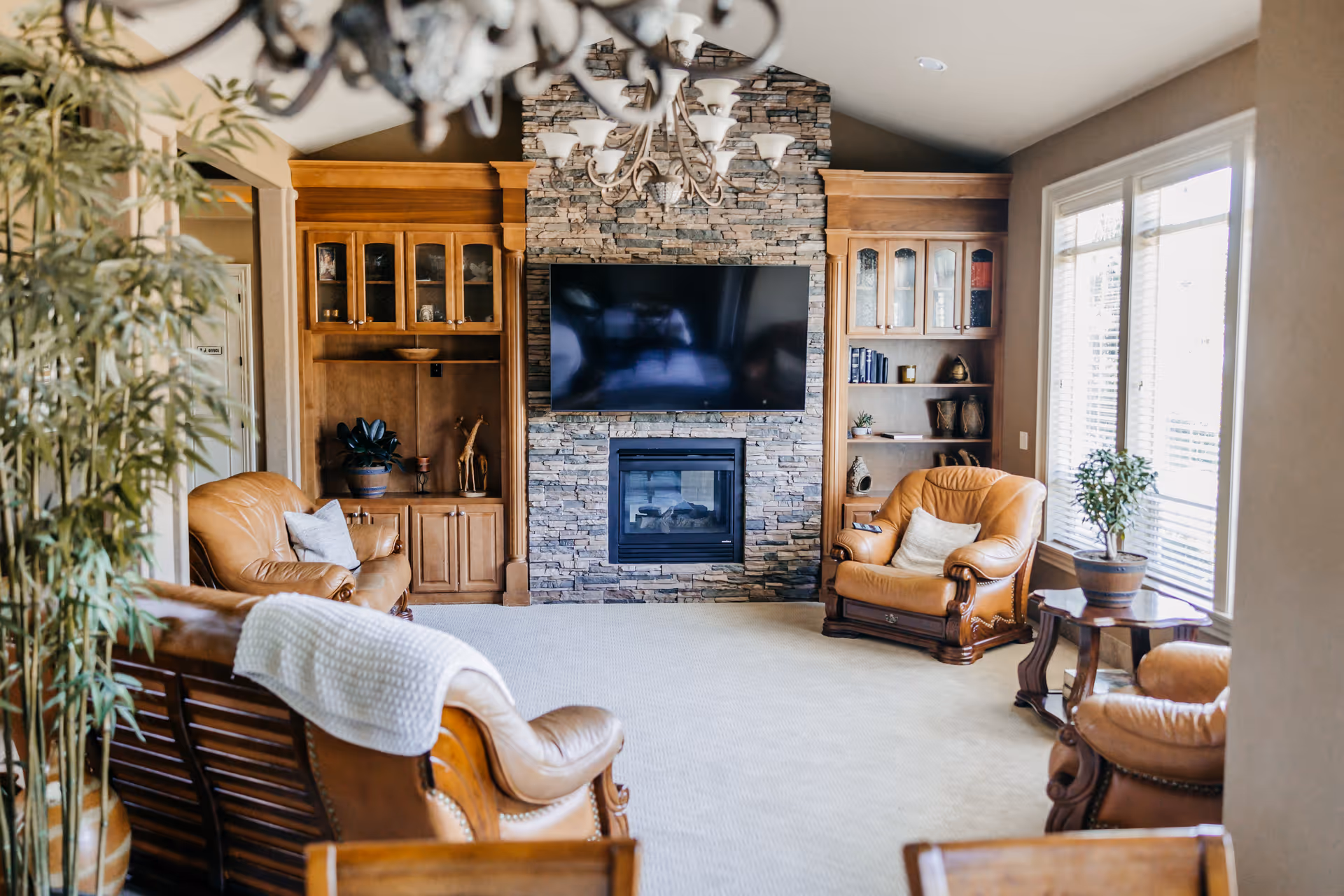 Cozy living room with leather seating, stone fireplace, built-in shelves, and a TV.
