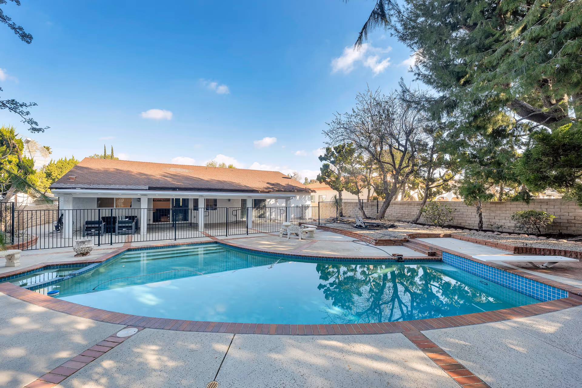 Outdoor pool area with lounge chairs, a single-story building, and trees surrounding.