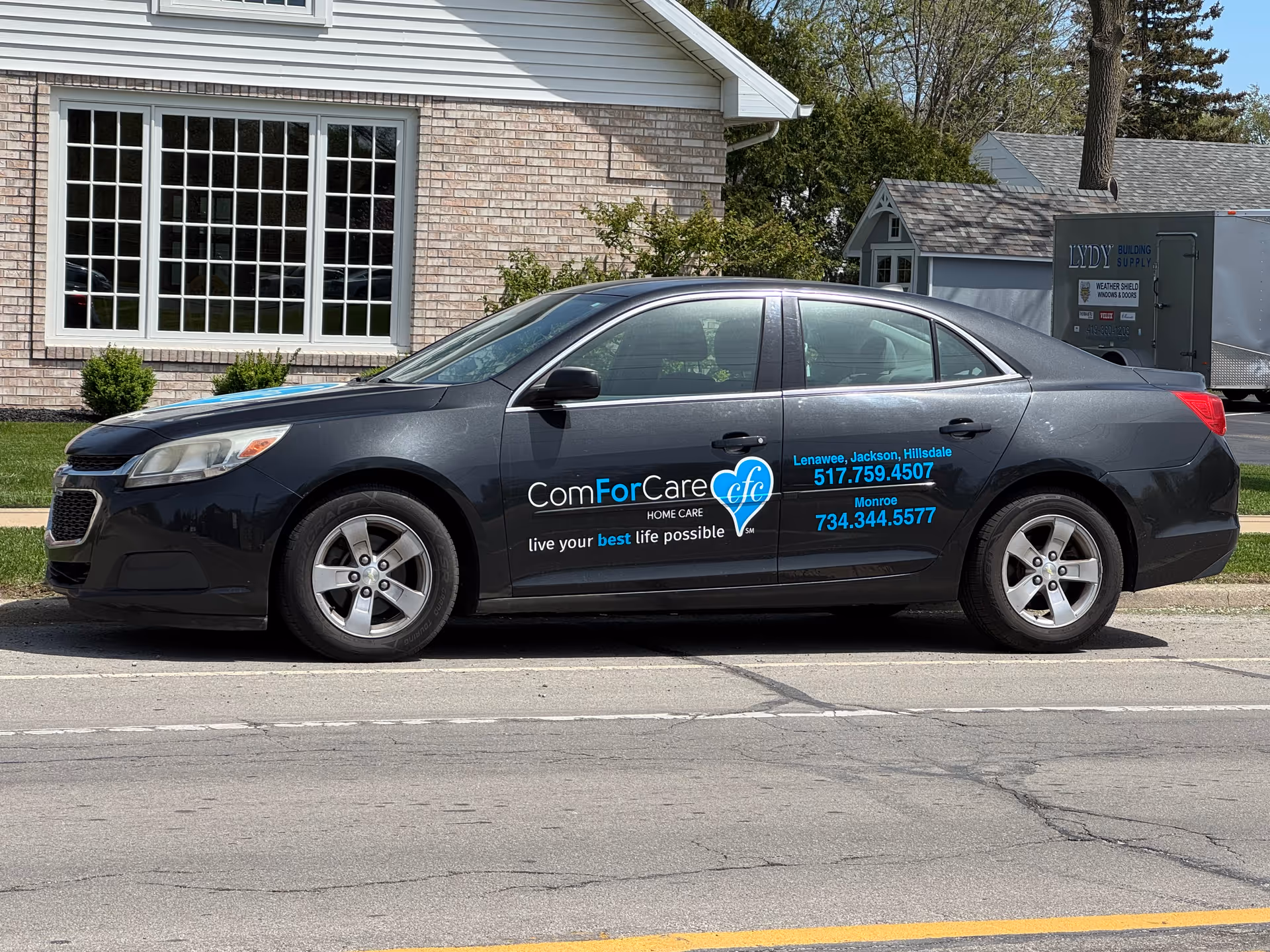 A ComForCare home care branded car sits in front of a brick building with large windows.