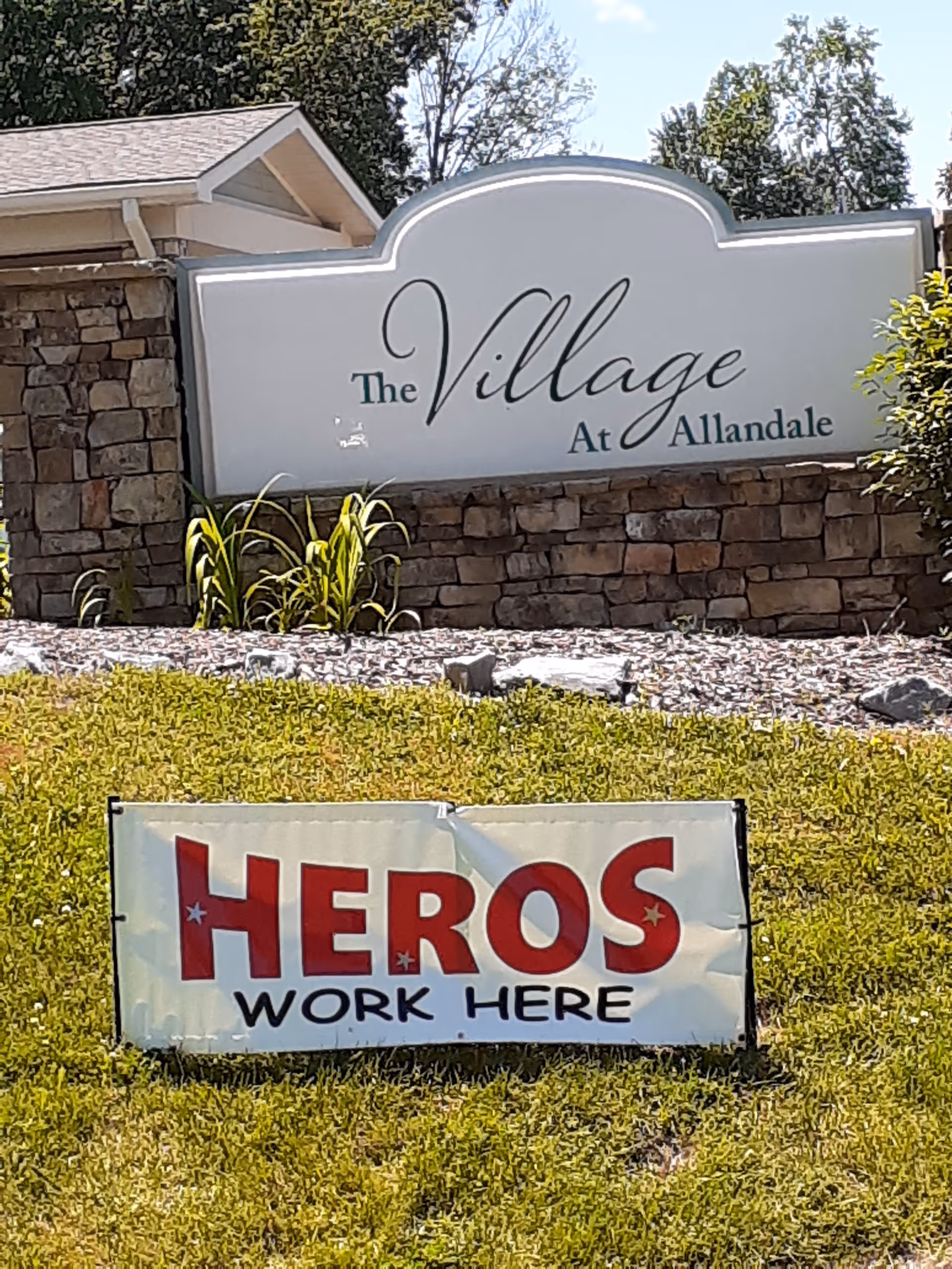 Stone entrance sign for The Village At Allandale with a Heroes Work Here banner