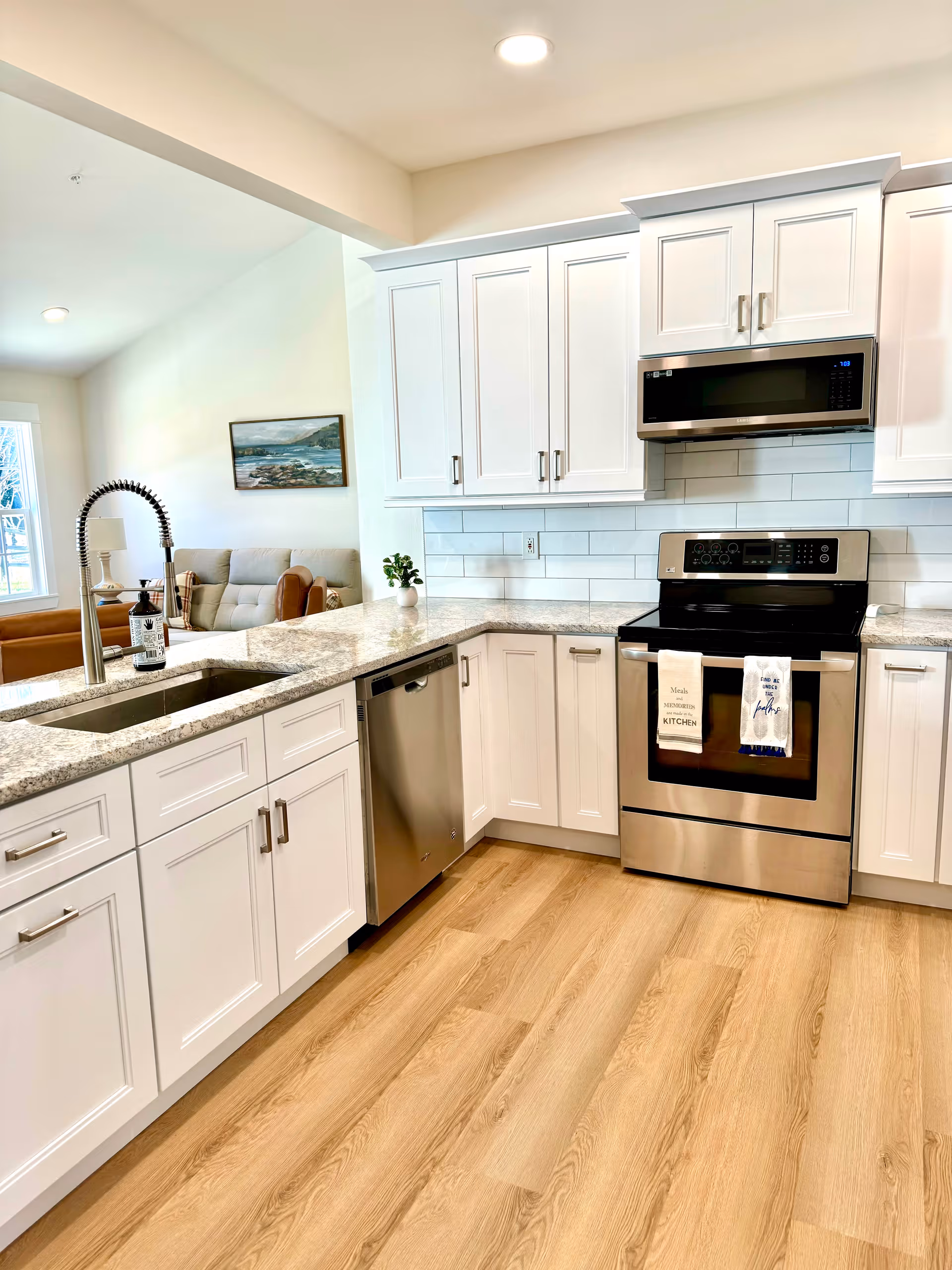 Bright white kitchen with stainless appliances and granite counters in an open-plan living area.