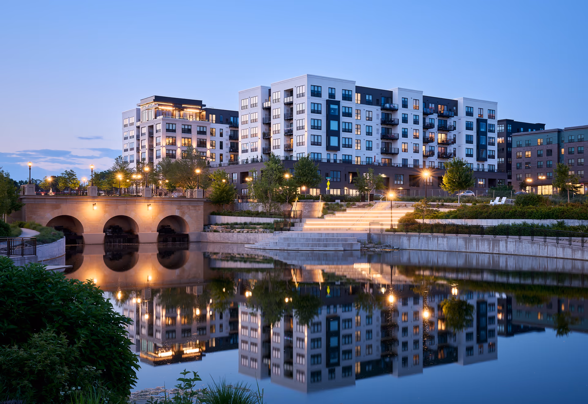 Modern multi-story senior living building by a waterfront with lights reflecting in water.
