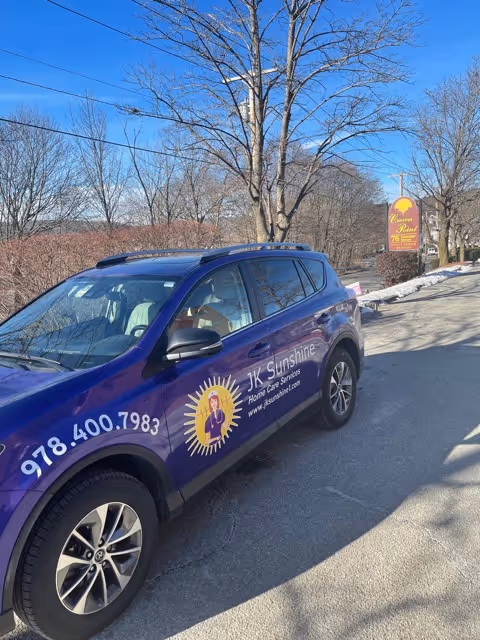 Purple JK Sunshine van parked on street displaying sun logo and contact numbers