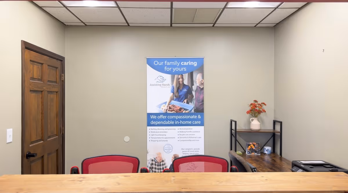An interior reception area with a banner, wooden desk, red chairs, and a small shelf.