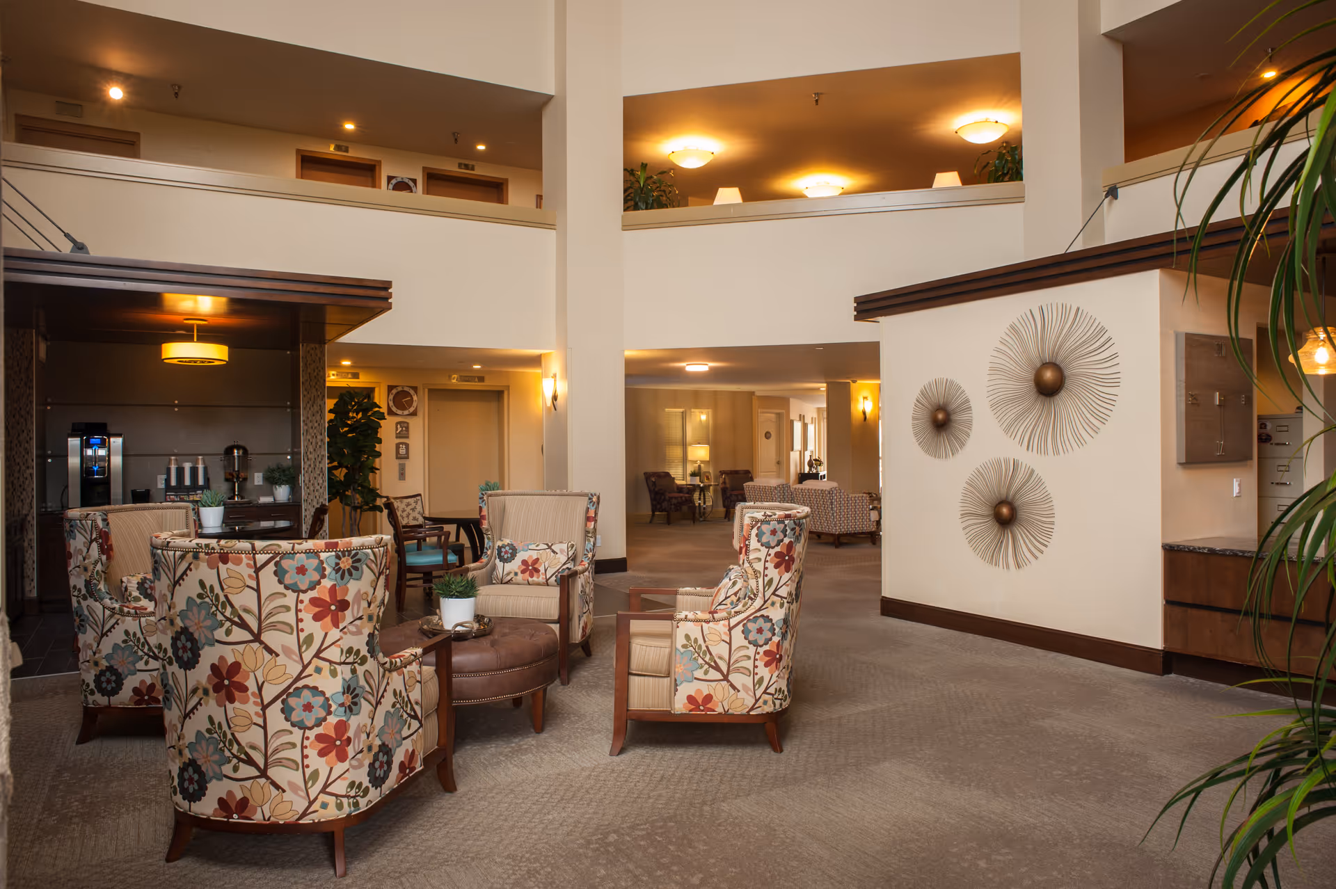Interior lounge area with floral upholstered chairs, tables, plants, and wall decor in a lobby.