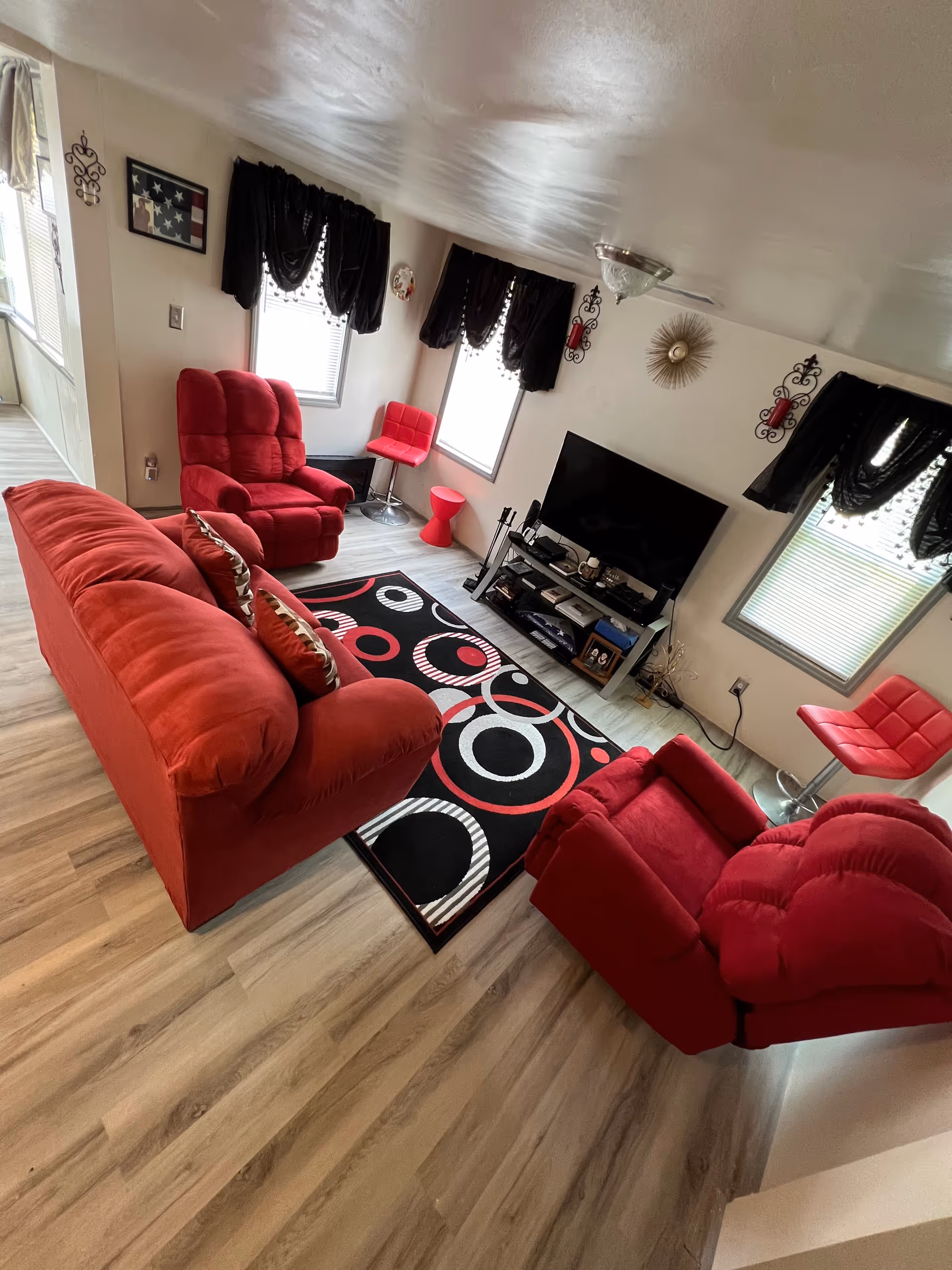 Red upholstered living room with sofa, chairs, a rug, windows, and a TV setup.