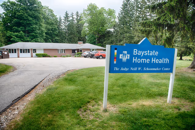Exterior view of Baystate Home Health facility with sign, driveway, and trees.