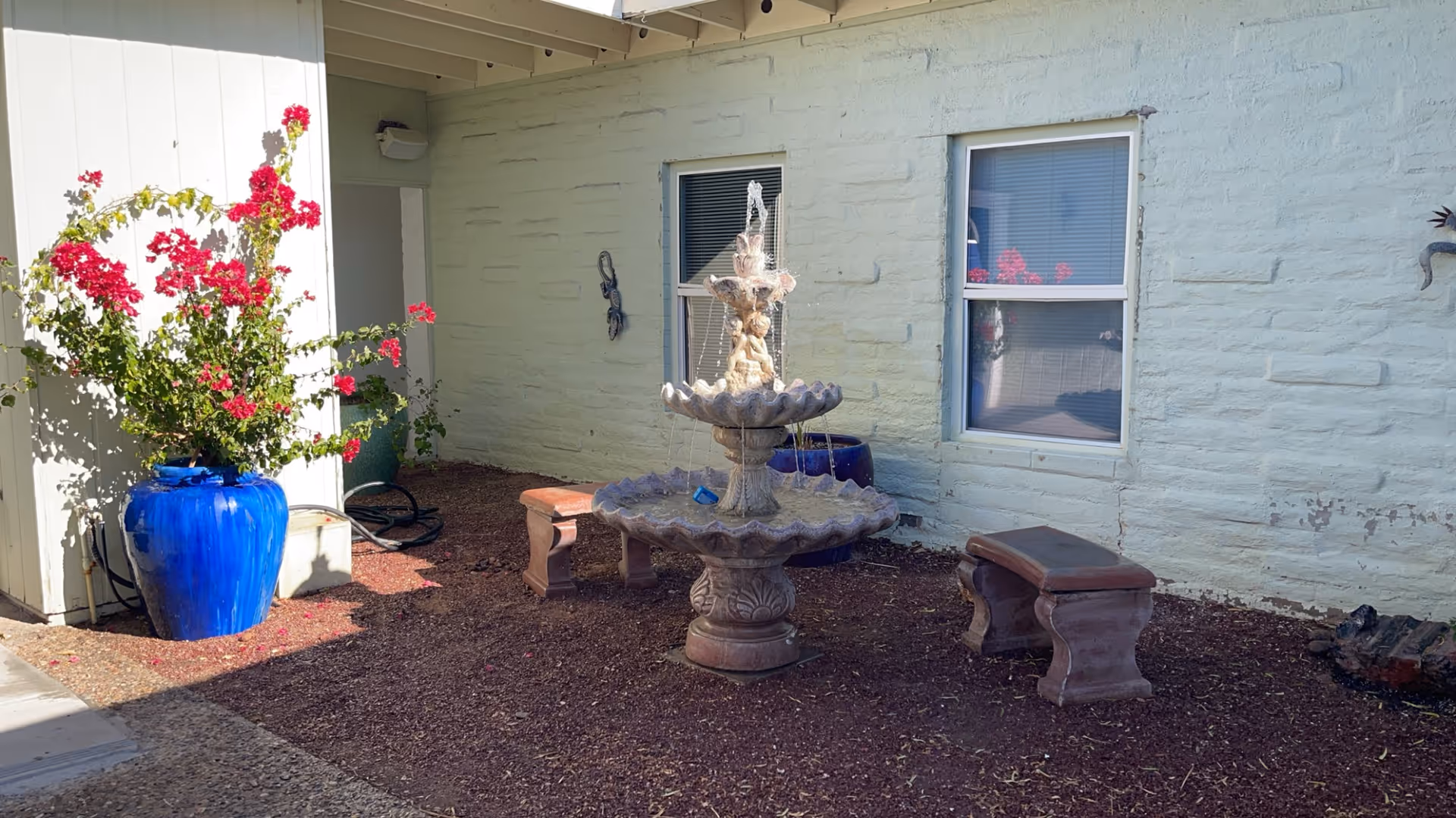Outdoor courtyard with fountain, benches, and a large blue pot with pink flowering plant.