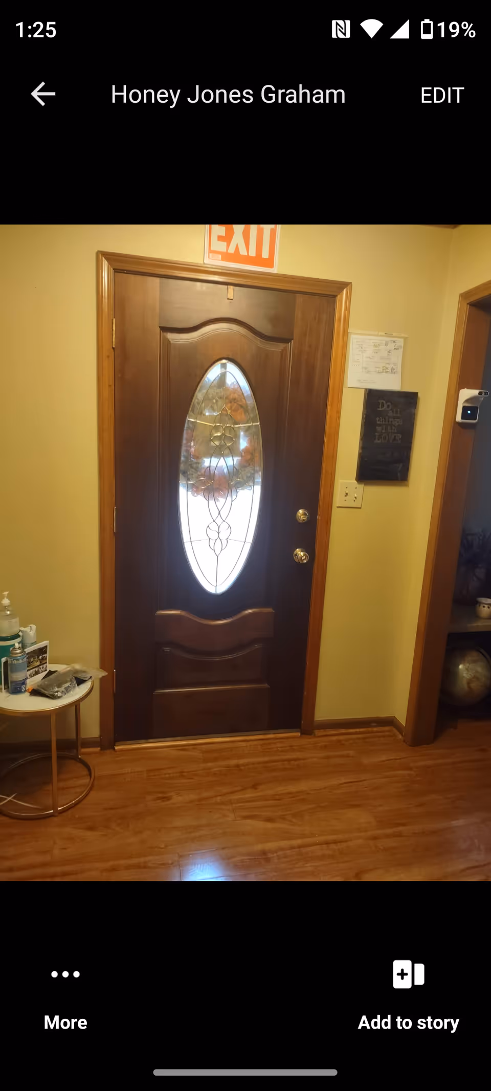 Interior hallway with a wooden door, stained glass oval window, and an exit sign.