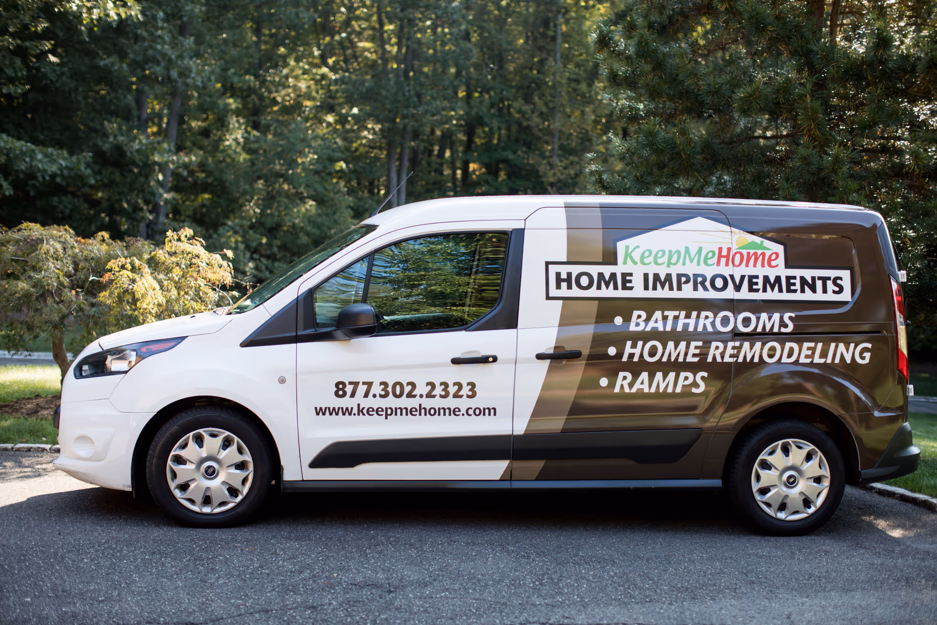 White KeepMeHome van parked on asphalt with logo and contact details.