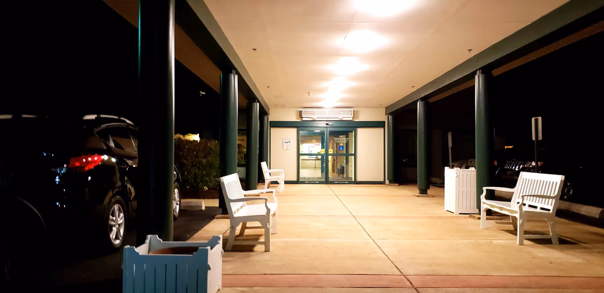 Nighttime exterior view of Naamans Creek Country Manor entrance with white benches along walkway