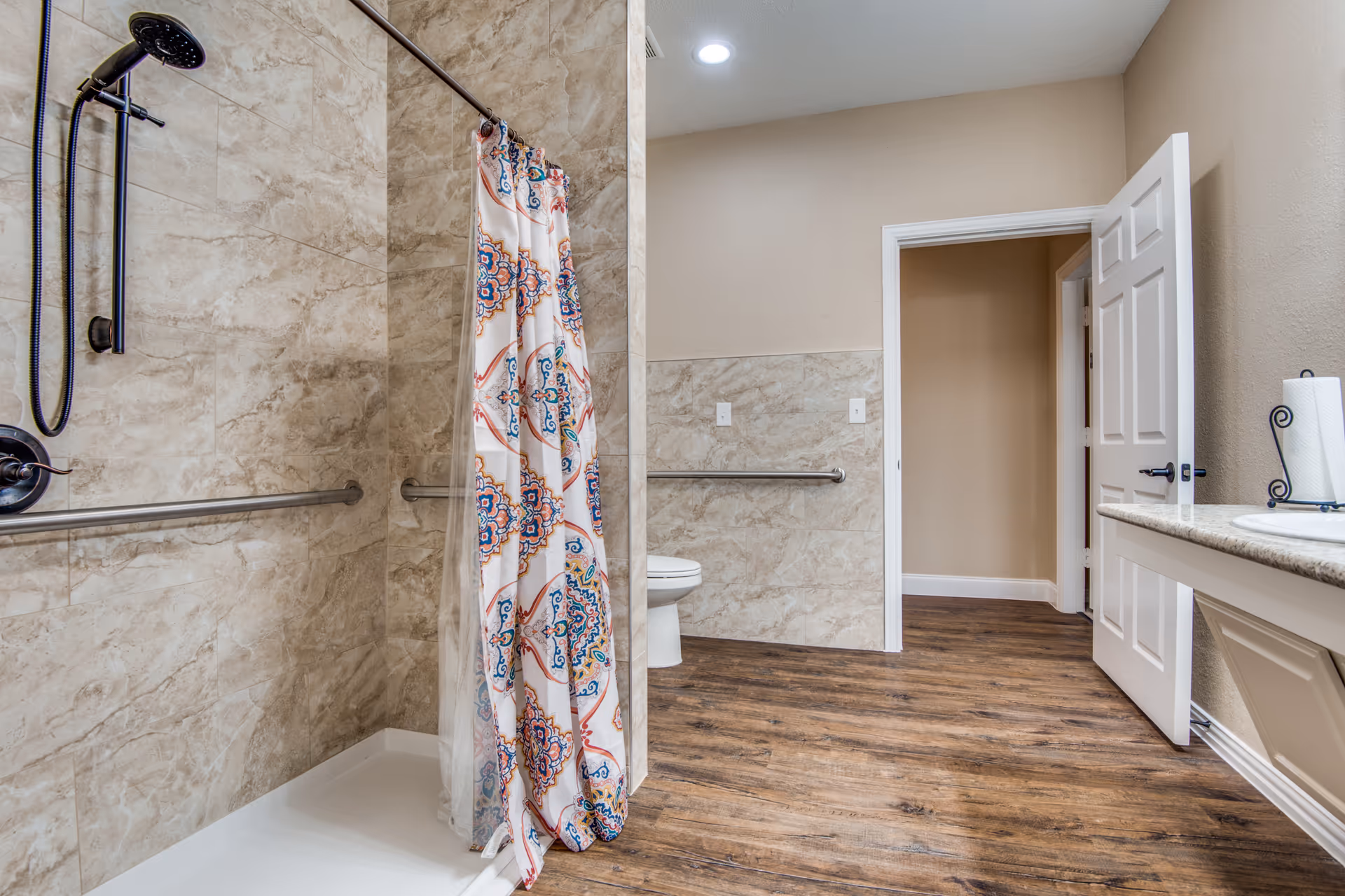 Accessible bathroom with shower, toilet, grab bars, and countertop in a senior facility.