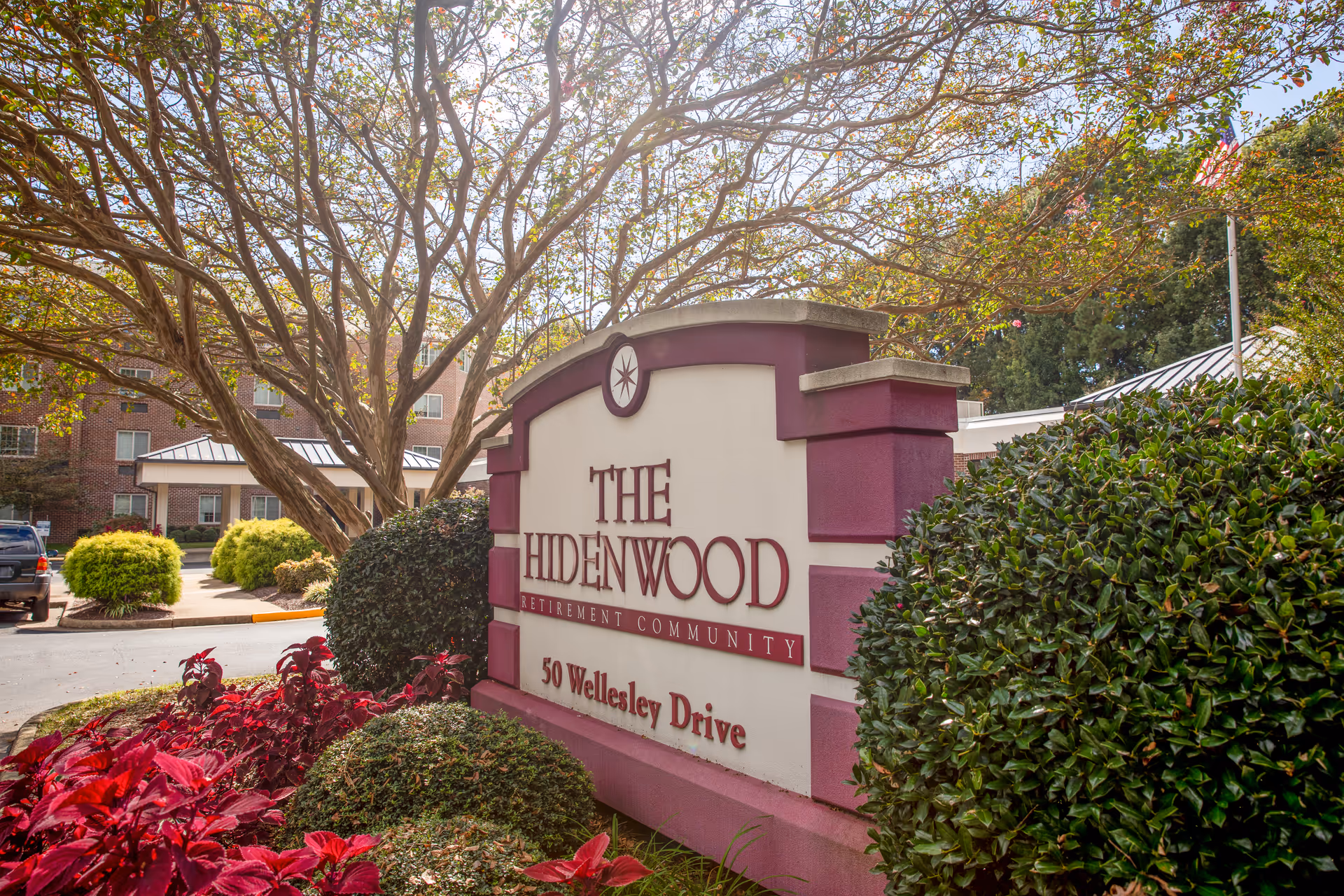 An entrance sign reading The Hidenwood Retirement Community surrounded by shrubs and trees.
