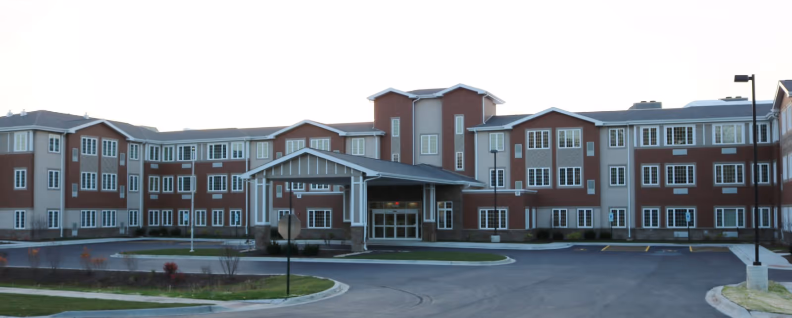 Exterior view of a multi-story senior living building with a covered entrance and parking lot.