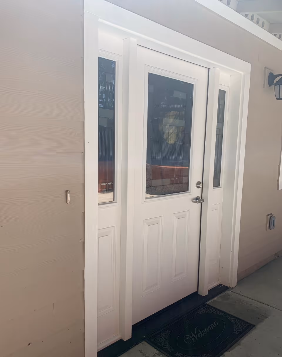 White exterior front door with decorative glass sidelights and a 'Welcome' doormat at the entrance.