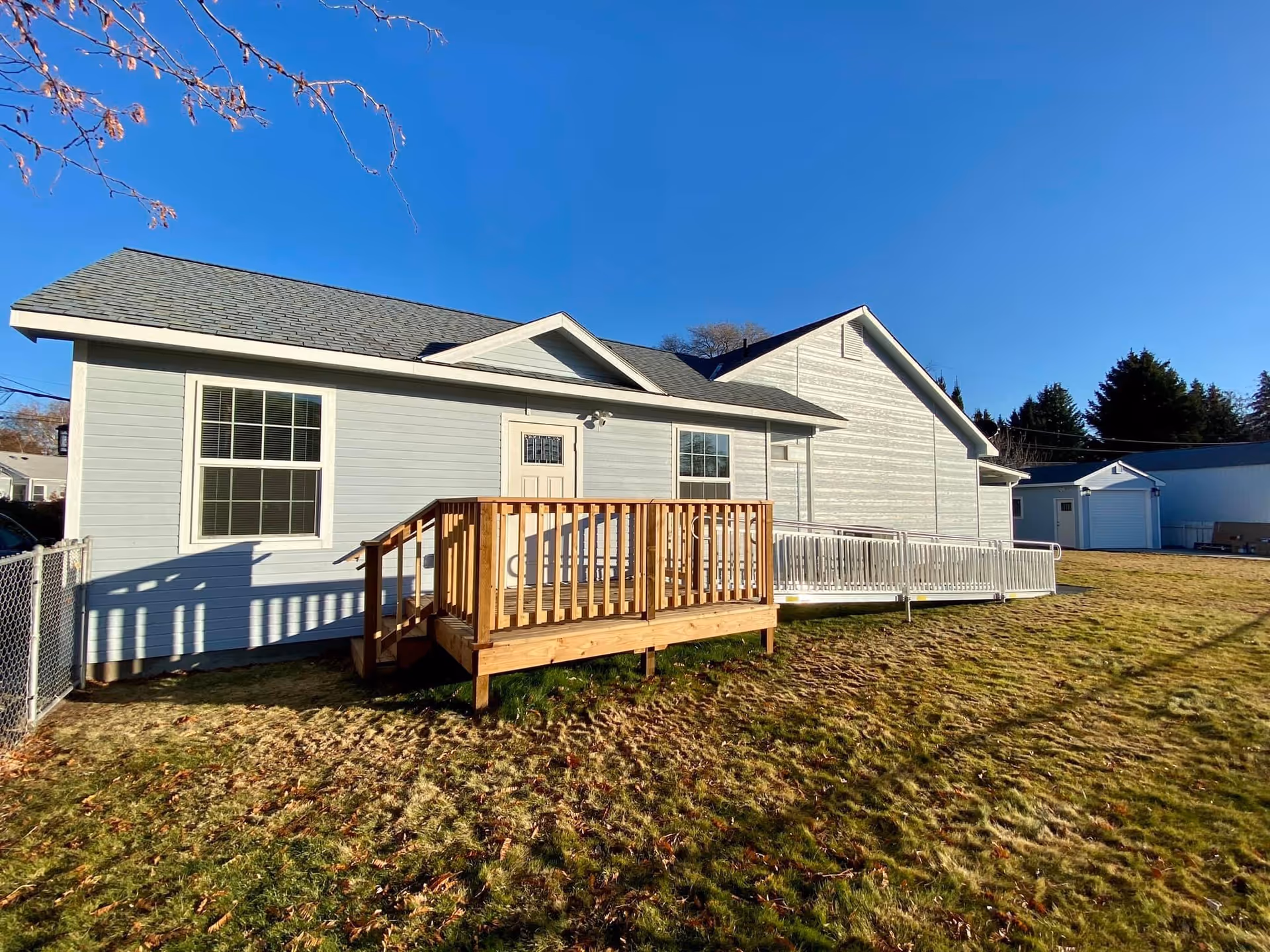 Single-story light-gray building with a wooden deck ramp, set on a grassy yard.