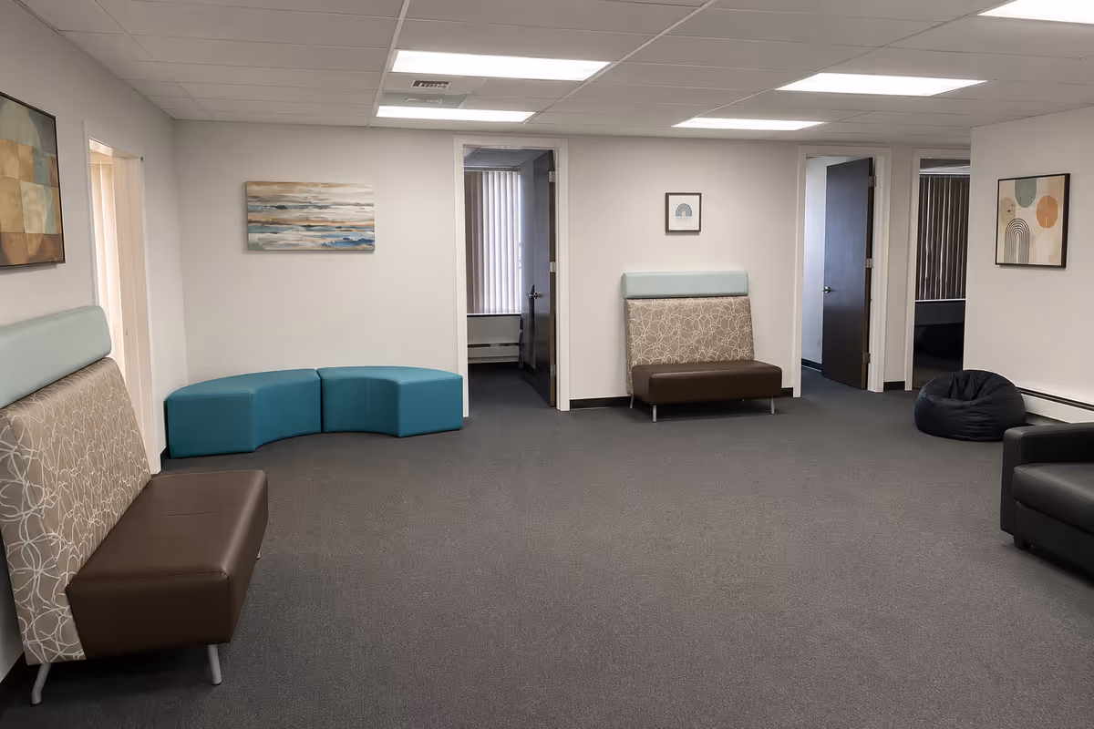 Spacious senior living lounge with beige patterned seating and teal modular chairs.