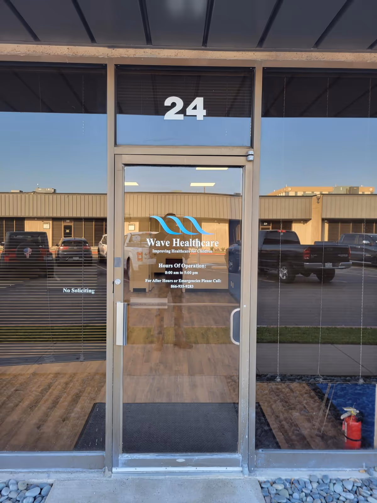 Glass entrance door with Wave Healthcare logo, building front and parking lot reflection.