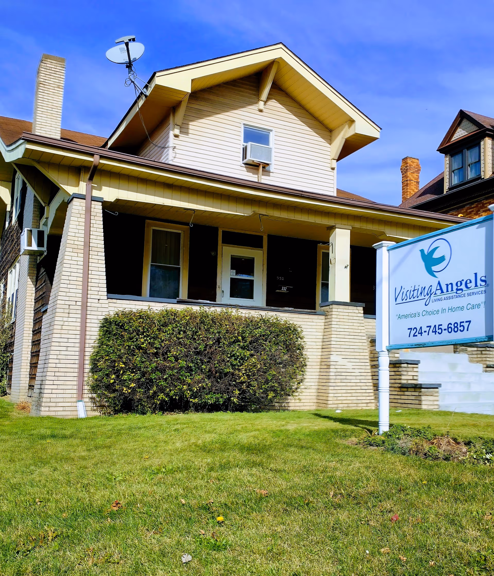 Front exterior of a beige senior care home with a blue Visiting Angels sign.