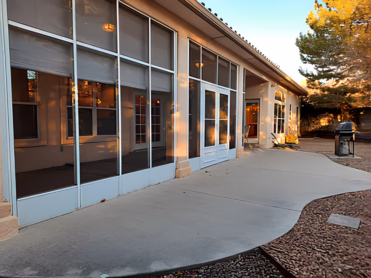 Exterior patio area with large glass windows and doors along a single-story building and a concrete walkway.