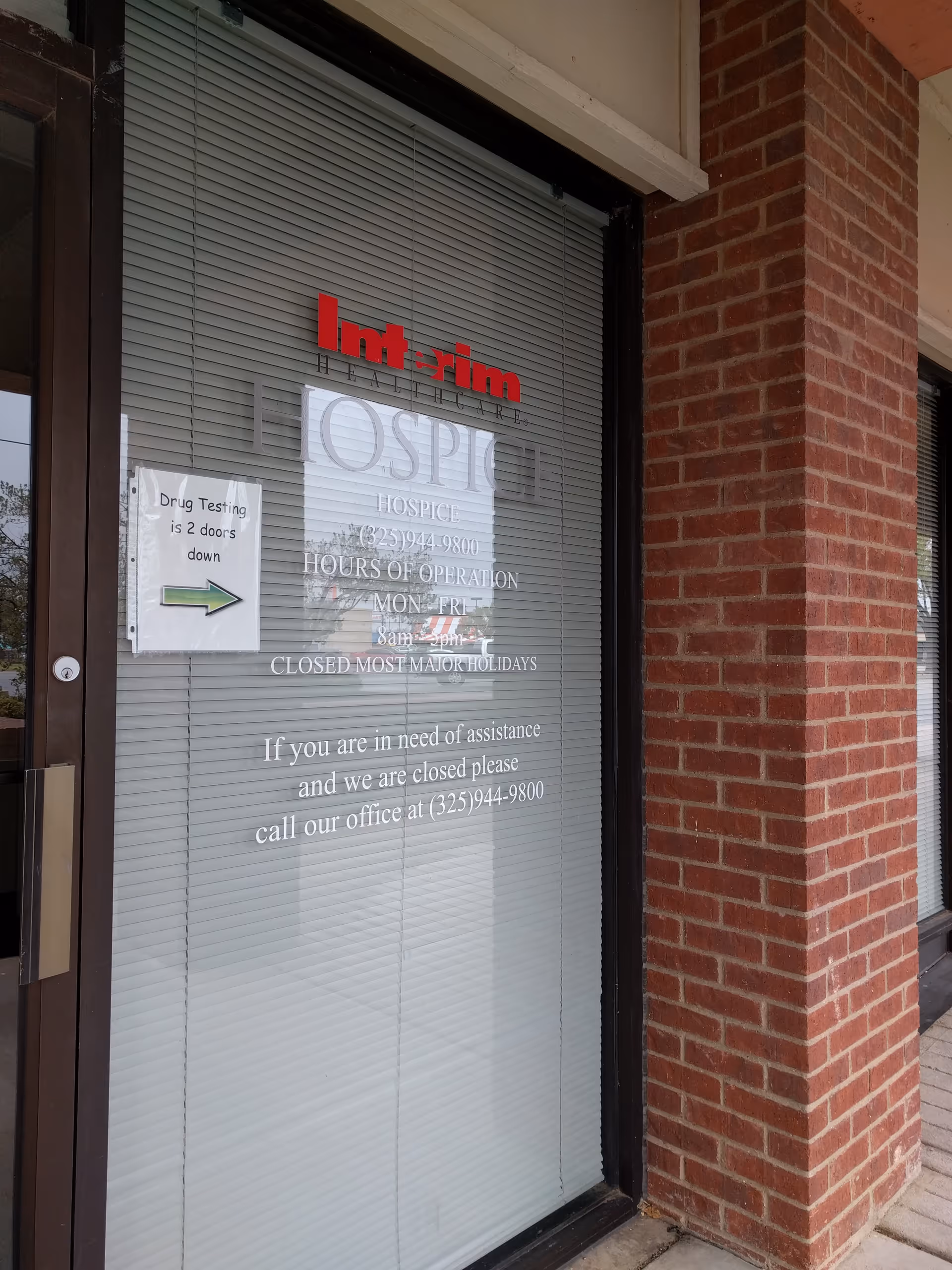 Glass storefront with blinds and red Interim HealthCare sign at a brick building entrance.