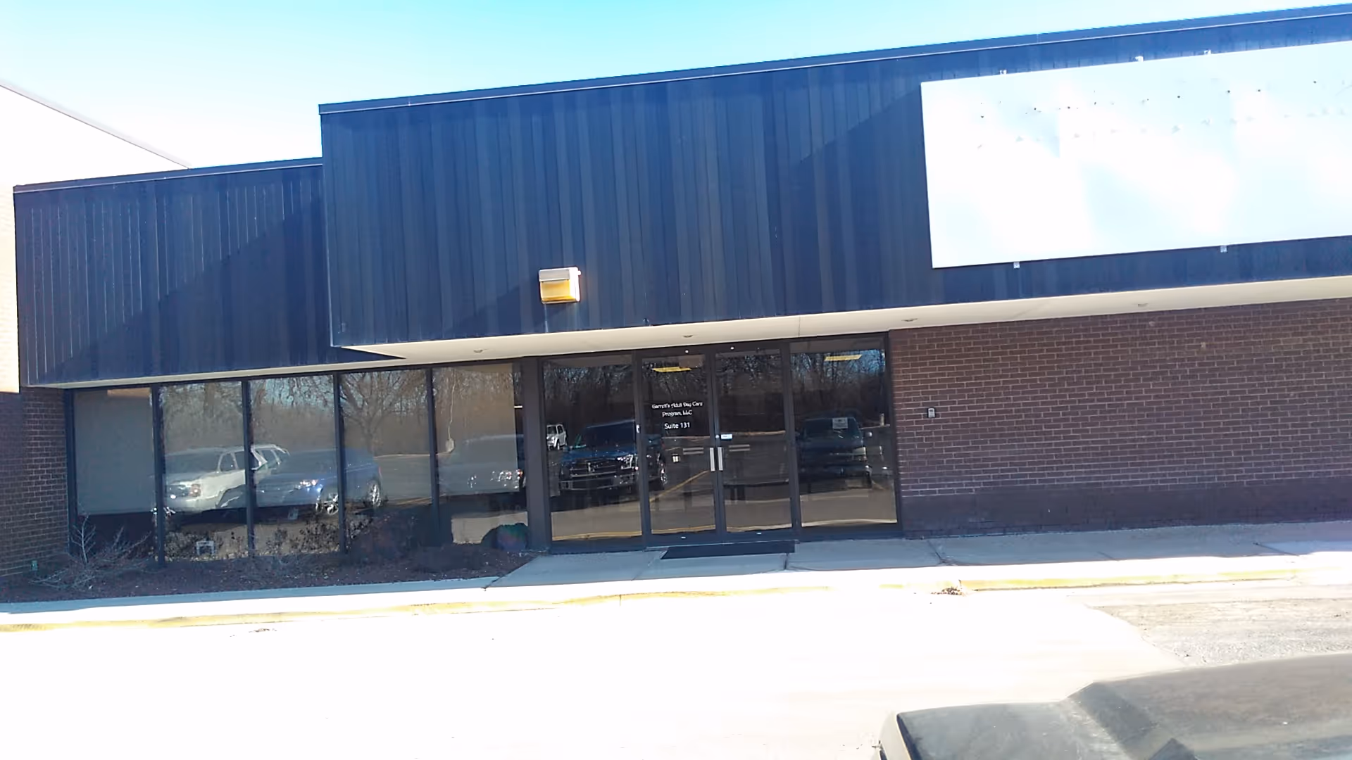 Exterior view of a blue brick facility with glass entry doors and a sidewalk.