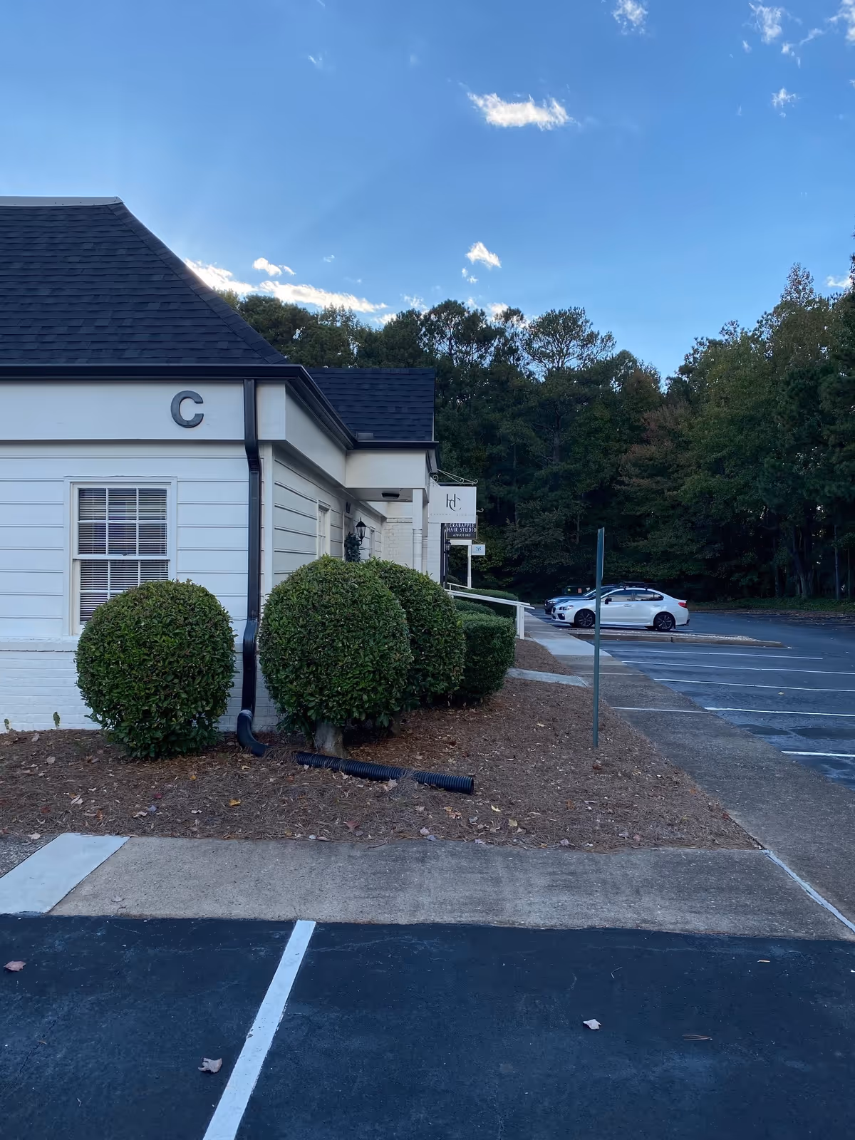 White building exterior with trimmed bushes and a parking lot under blue sky.