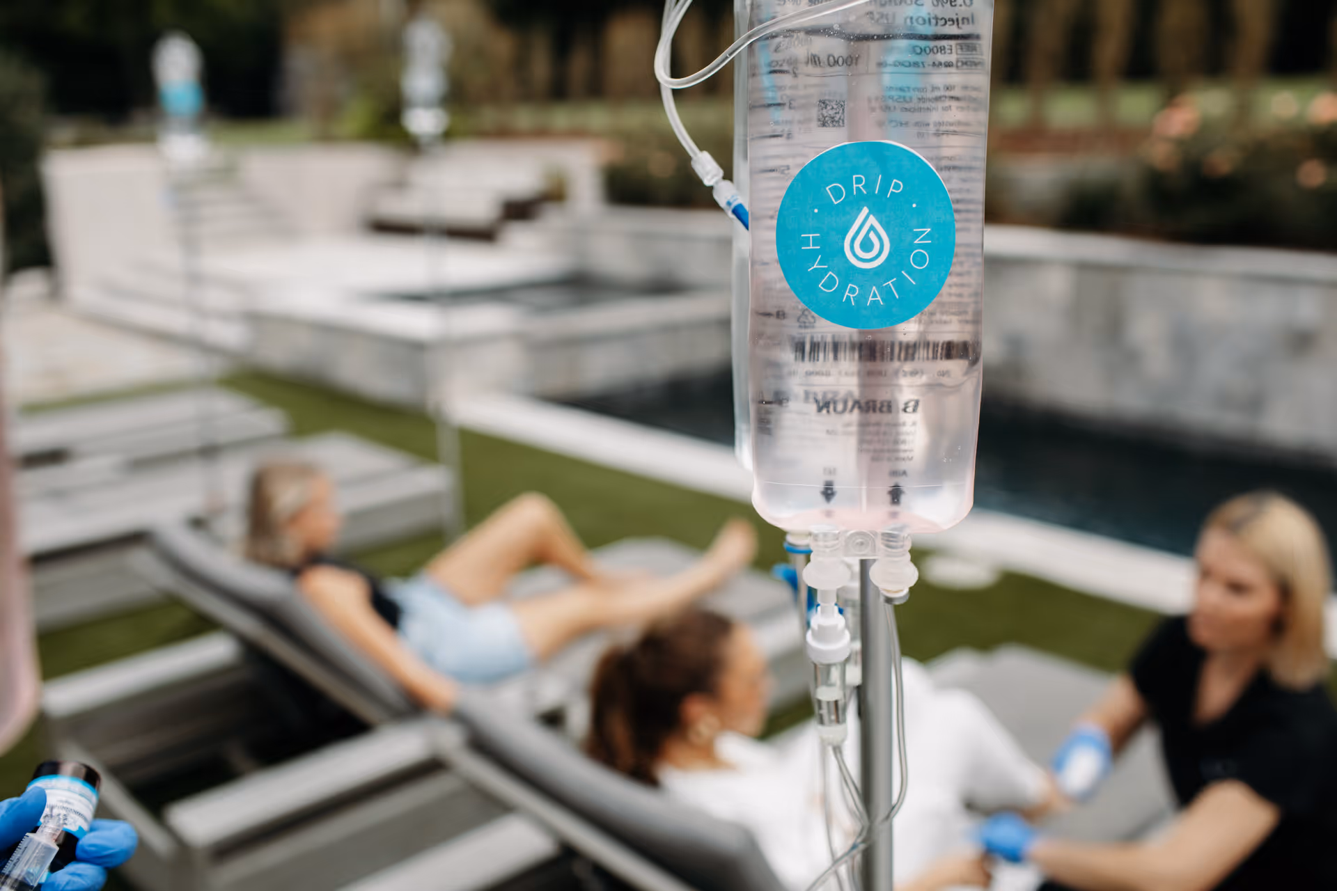 Outdoor poolside scene with an IV hydration drip labeled Drip Hydration and lounging residents.